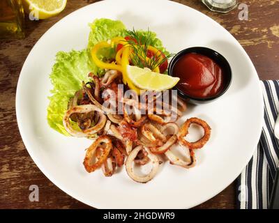 Krake, gebratene Calamari-Ringe mit Salat auf einem Teller mit Chilisauce und Zitrone Stockfoto