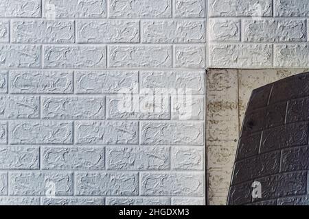 Die Tapete beginnt sich abzulösen. Die Tapete aus alten weißen Ziegeln schälte sich von der Wand im Raum, weil es feucht war oder sich nicht gut klebte. Reparieren Sie A Stockfoto