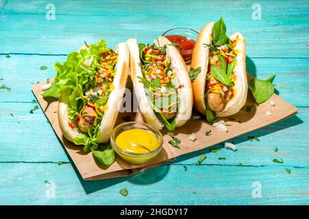 Hausgemachte vegane Hotdogs. Hot Dog mit weißen Fleischwürsten, frischem Gemüse, Grüns, Saucen, im Sommer Sonne beleuchtet blauen Holzhintergrund Kopierraum Stockfoto