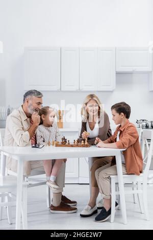 Glückliche Großeltern spielen Schach mit Kindern in der Küche Stockfoto