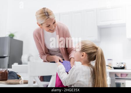 Fröhliche Frau hält die Lunchbox in der Nähe der Enkelin und ein Glas mit Schokoladenpaste in der Küche Stockfoto