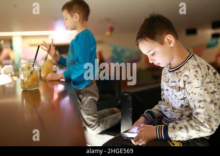 Kind mit Smartphone in der Bar des Restaurants am Abend Stockfoto