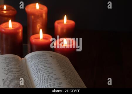 Öffne die christliche bibel und brennende rote Kerzen in einem dunklen Raum mit Kopierraum Stockfoto