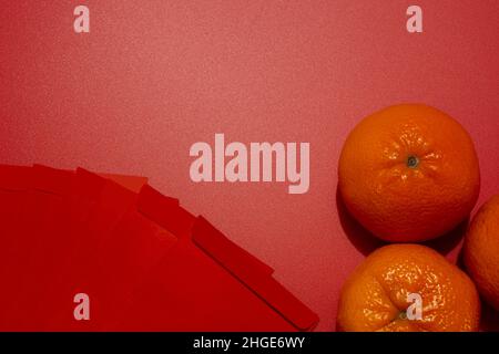 Chinesisches Neujahrskonzept – Mandarin-Orangen und rote Päckchen auf rotem Hintergrund Stockfoto