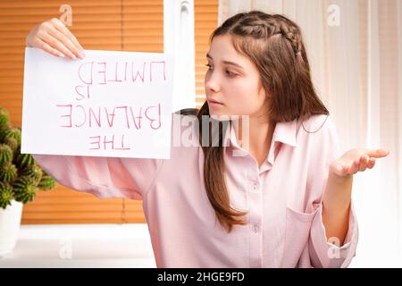 Junge hübsche Frau, die verzweifelt ihre Haltung gegenüber Zahlungsrechnungen zeigt und ein Papier mit einer Inschrift auf dem Kopf hält. Stockfoto