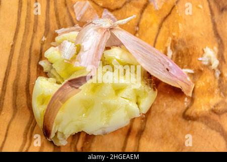 Zerdrückte Knoblauchzehe in einem Sandelholz-Schneidebrett Stockfoto