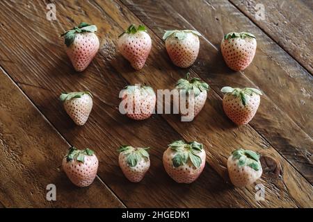 Frisches Obst Flach Legen. 3 Reihen von Pineberries auf Holztisch. Weiße Erdbeeren. Stillleben Von Saisonalen Früchten. Rosa und weiße Beeren auf dunklem Hintergrund. Stockfoto