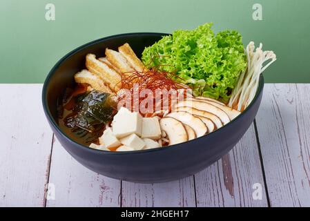 Koreanischer Ramen würziger Miso mit Schweinefleisch, Ei und Pilzen, Gemüse in einer blauen Schüssel auf einem Holztisch Stockfoto