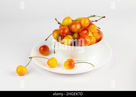 Reife süße rainier Kirschen in einer weißen Schale und auf einem Teller auf weißem Hintergrund. Stockfoto