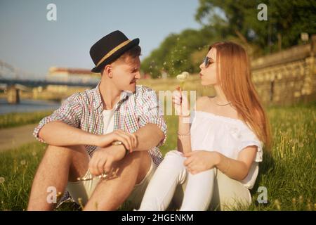 Paar in der Liebe Blasen Blowballs Blumen in die Gesichter von einander. Lächelnde und lachende Menschen, die sich an einem warmen Sommertag draußen gut amüsiert haben. Allergie gegen f Stockfoto