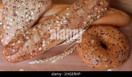 Verschiedene Brotsorten, frisches Gebäck in der Bäckerei. Brot mit Sesam, Getreide, Samen. Verschiedene Formen und Arten von Rollen. Weizenohren auf einem W Stockfoto