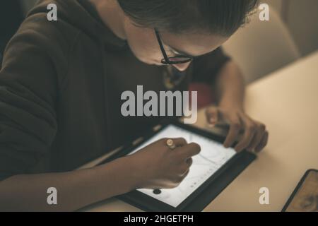 Teenager zeichnen mit Tablet und virtuellem Stift. Schüler der Millennials machen Hausaufgaben mit neuen Technologiegeräten. Kleiner Junge zeichnen auf Pad zu Hause. Männliche Hände Stockfoto