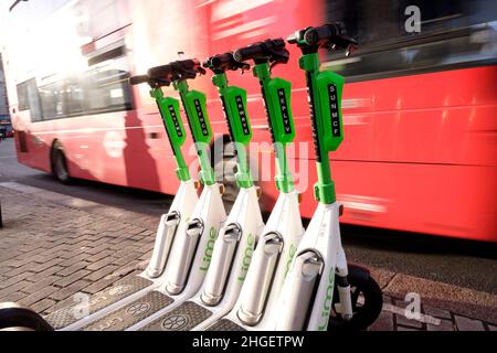 Ein Londoner Bus fährt an einer Reihe von Elektrorollern vorbei, die in einer dedizierten Bucht im Zentrum von London, Großbritannien, gemietet werden können Stockfoto