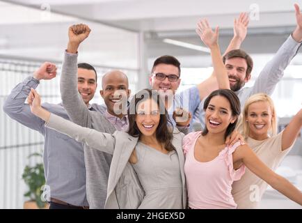 Feiern wir den Erfolg. Ausgeschnittene Aufnahme einer Gruppe von Geschäftsleuten, die lächeln und die Hände heben. Stockfoto