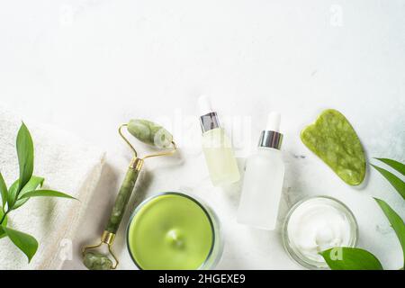 Jade Roller und Gua Sha Stone Massagegerät mit Gesichtscreme und Serumflasche. Stockfoto