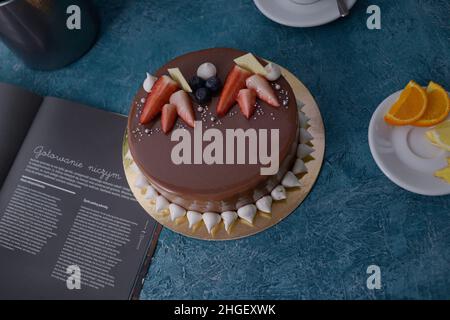 Schokoladenkuchen mit Erdbeeren. Blumen Tulpen, grüner Tee, Zitrone und Orange. Desserts auf blauem Hintergrund. Food-Foto. Kuchen auf Bestellung. Stockfoto
