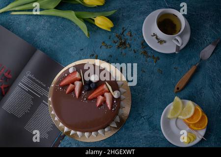 Schokoladenkuchen mit Erdbeeren. Blumen Tulpen, grüner Tee, Zitrone und Orange. Desserts auf blauem Hintergrund. Food-Foto. Kuchen auf Bestellung. Stockfoto