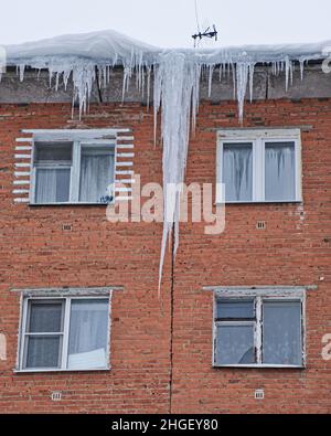 Riesige Eiszapfen, die vom Dach eines alten Backsteinhauses herabhängen. Gefährliche Eiszapfen hängen vom Dach. Harter winter im norden. Stockfoto