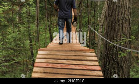 Wandern im grünen tropischen Dschungel, Mittelamerika. Rückansicht eines Mannes mit einer metallenen Thermoskanne in der Hand, der die hölzerne Hängebrücke umgab b Stockfoto