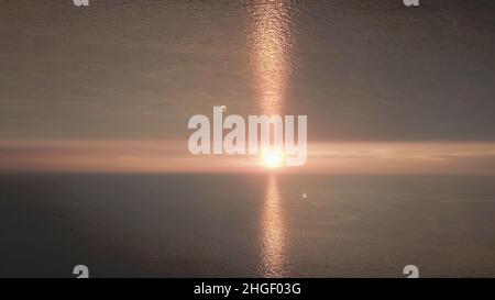 Schöner Sonnenuntergang im Meer mit einem Spiegelhorizont-Effekt. Abendsonne am Horizont mit Lichtes, Aufbruchthema Stockfoto