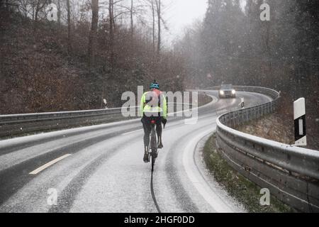 Bielefeld, Deutschland. 20th Januar 2022. Ein Radfahrer fährt auf einer leicht verschneiten Straße im Teutoburger Wald. Schnee und Sonne wechseln sich in Teilen Ostwestfalens bei Temperaturen um den Gefrierpunkt ab. Quelle: Friso Gentsch/dpa/Alamy Live News Stockfoto