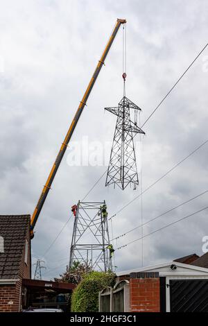 Arbeiter lösen die obere Hälfte eines elektrischen Masten, der von der Basis mit einem Kran zur Wartung am Boden angehoben wird Stockfoto