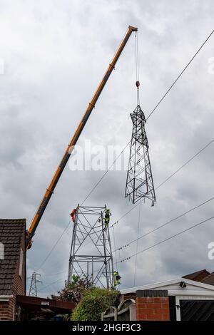 Arbeiter lösen die obere Hälfte eines elektrischen Masten, der von der Basis mit einem Kran zur Wartung am Boden angehoben wird Stockfoto