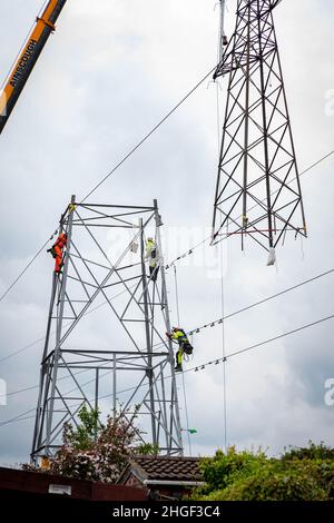 Arbeiter lösen die obere Hälfte eines elektrischen Pylons, der zur Wartung mit einem Kran auf den Boden abgesenkt wird Stockfoto