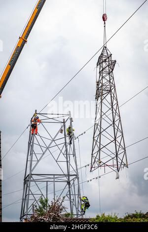 Arbeiter lösen die obere Hälfte eines elektrischen Pylons, der zur Wartung mit einem Kran auf den Boden abgesenkt wird Stockfoto