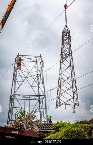 Arbeiter lösen die obere Hälfte eines elektrischen Pylons, der zur Wartung mit einem Kran auf den Boden abgesenkt wird Stockfoto