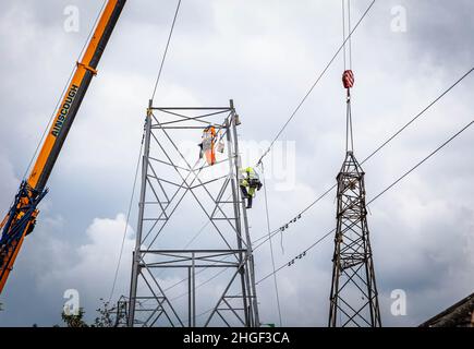 Arbeiter lösen die obere Hälfte eines elektrischen Pylons, der zur Wartung mit einem Kran auf den Boden abgesenkt wird Stockfoto