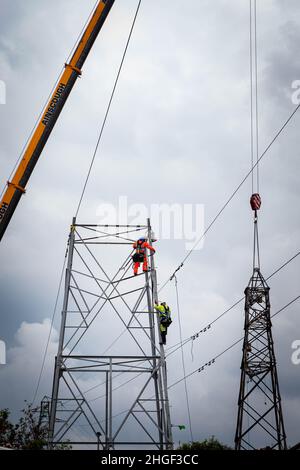 Arbeiter lösen die obere Hälfte eines elektrischen Pylons, der zur Wartung mit einem Kran auf den Boden abgesenkt wird Stockfoto