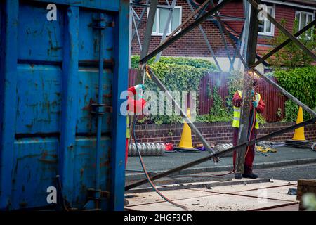 Arbeiter in PSA verwenden oxyde Acetylenbrenner, um beschädigte Teile eines geerdeten Strommasylons auszuschneiden Stockfoto