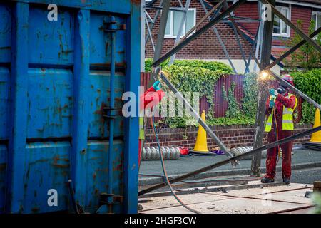 Arbeiter in PSA verwenden oxyde Acetylenbrenner, um beschädigte Teile eines geerdeten Strommasylons auszuschneiden Stockfoto