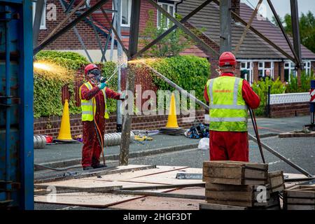 Arbeiter in PSA verwenden oxyde Acetylenbrenner, um beschädigte Teile eines geerdeten Strommasylons auszuschneiden Stockfoto