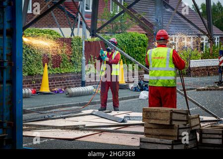 Arbeiter in PSA verwenden oxyde Acetylenbrenner, um beschädigte Teile eines geerdeten Strommasylons auszuschneiden Stockfoto