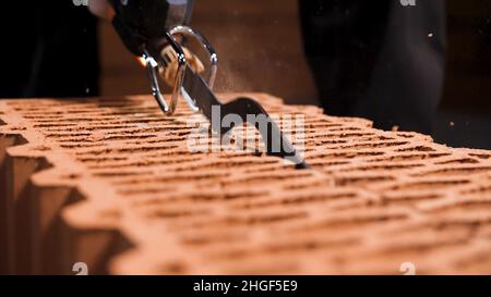 Nahaufnahme eines Mannes, der mit einer elektrischen Säge einen Block in einer Staubwolke durchschneidet. Details des neuen Backsteinhauses. Stockfoto