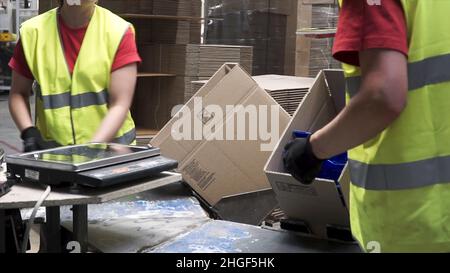 Nahaufnahme der Hände eines Fertigungsarbeiters, der verpackte Produkte in Kartons vor dem Export oder Versand während manueller Arbeiten in einem cos einlegt Stockfoto