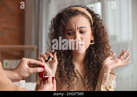 Enttäuschte junge afroamerikanische Frau, die den Verlobungsring ihres Freundes durch die Lupe zu Hause betrachtet Stockfoto