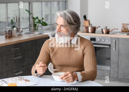 Älterer Mann, der in der Küche am Tisch gefrühstückt hat Stockfoto