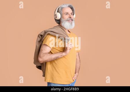 Älterer Mann mit kabellosen Kopfhörern auf beigefarbenem Hintergrund Stockfoto