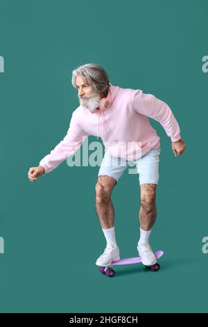 Senior Mann mit Skateboard auf grünem Hintergrund Stockfoto