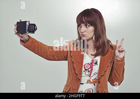 Das Selfie der Siebziger. Beschnittene Studioaufnahme einer jungen Frau in einem Vintage-Outfit, die mit einer altmodischen Kamera ein Selfie gemacht hat. Stockfoto