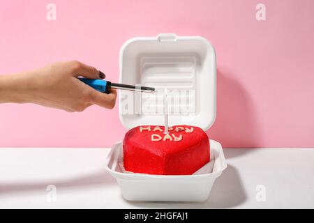 Frau zündet Kerze auf leckeren Bento-Kuchen am Tisch an Stockfoto