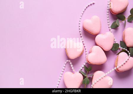 Leckere herzförmige Makronen mit Perlen und Ästen auf violettem Hintergrund Stockfoto