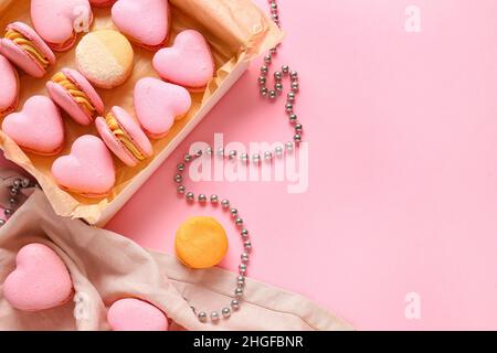 Box mit leckeren herzförmigen Makronen und Perlen auf rosa Hintergrund Stockfoto