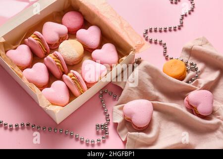 Box mit leckeren herzförmigen Makronen und Perlen auf rosa Hintergrund Stockfoto