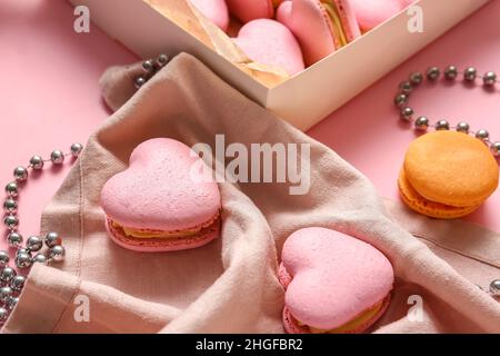 Leckere herzförmige Makronen und Perlen auf rosa Hintergrund, Nahaufnahme Stockfoto