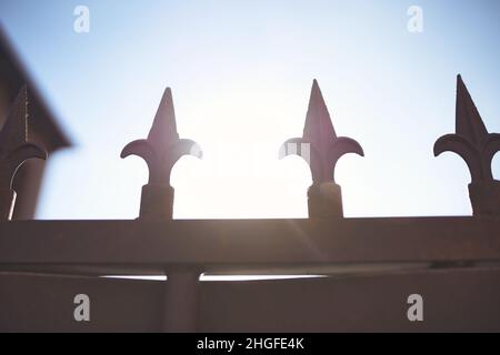 Schmiedeeiserne Stacheln an einem Tor mit der Sonne im Hintergrund. Stockfoto