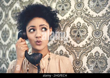 Oh, wirklich. Studioaufnahme einer jungen Frau in einem Vintage-Outfit, die auf einem altmodischen Telefon spricht. Stockfoto